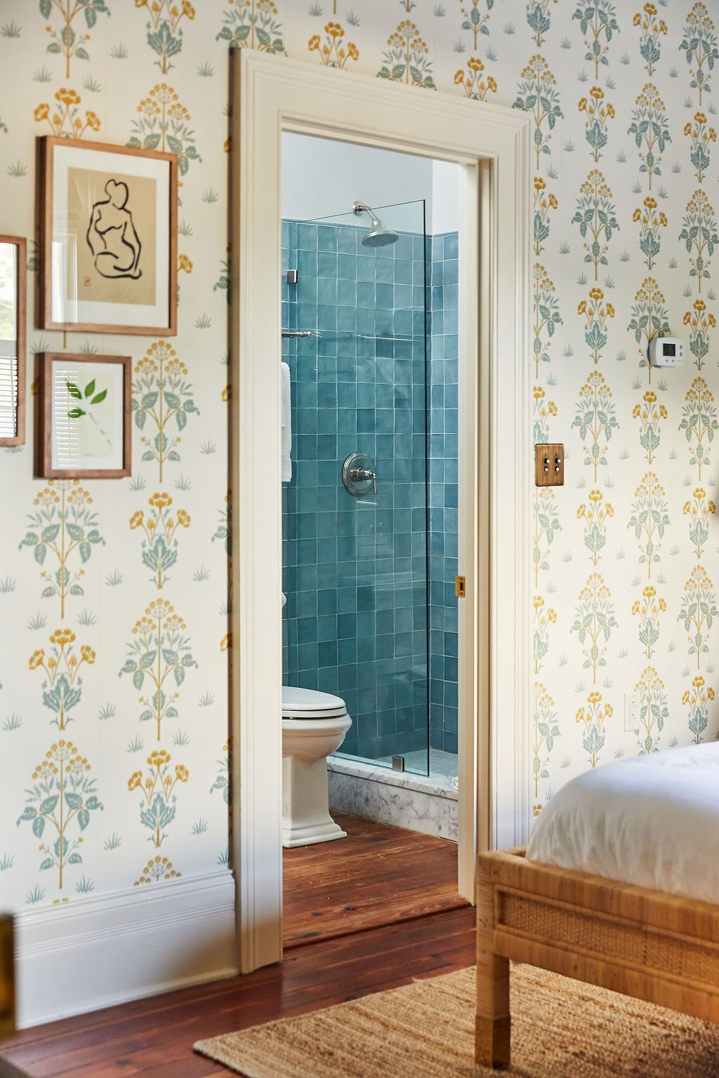 A bedroom with a wooden bed, a wooden floor, a white door leading to a bathroom with a shower and toilet.