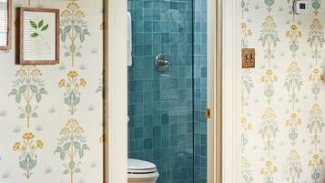 A bedroom with a wooden bed, a wooden floor, a white door leading to a bathroom with a shower and toilet.