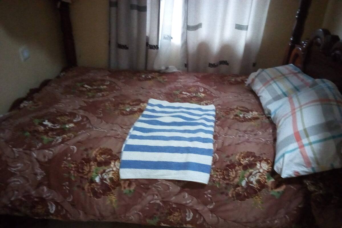 A bed with a floral-patterned bedspread, a striped towel, and a plaid pillow.