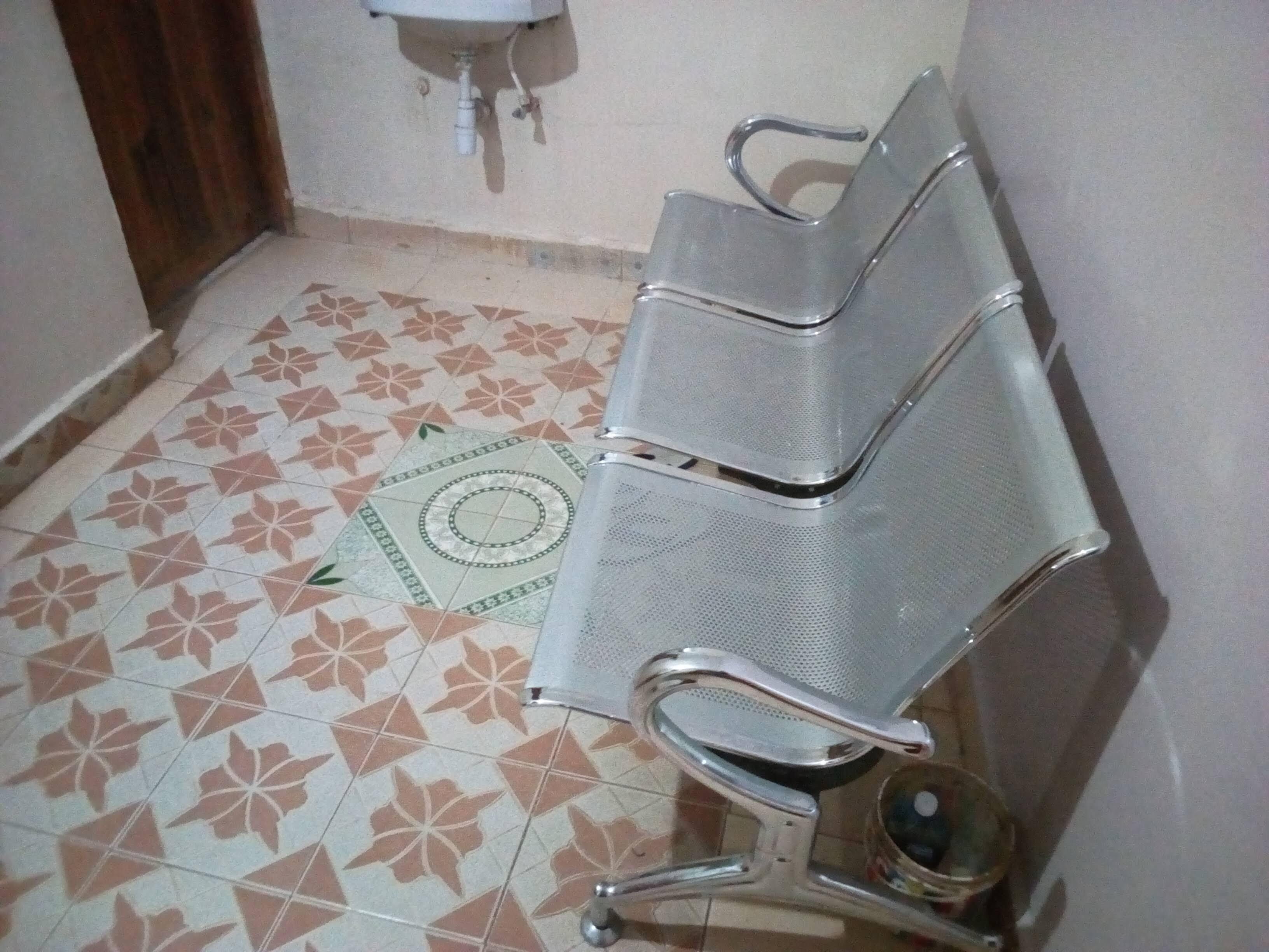 Een badkamer met betegelde vloer, een wastafel en een metalen bankje.