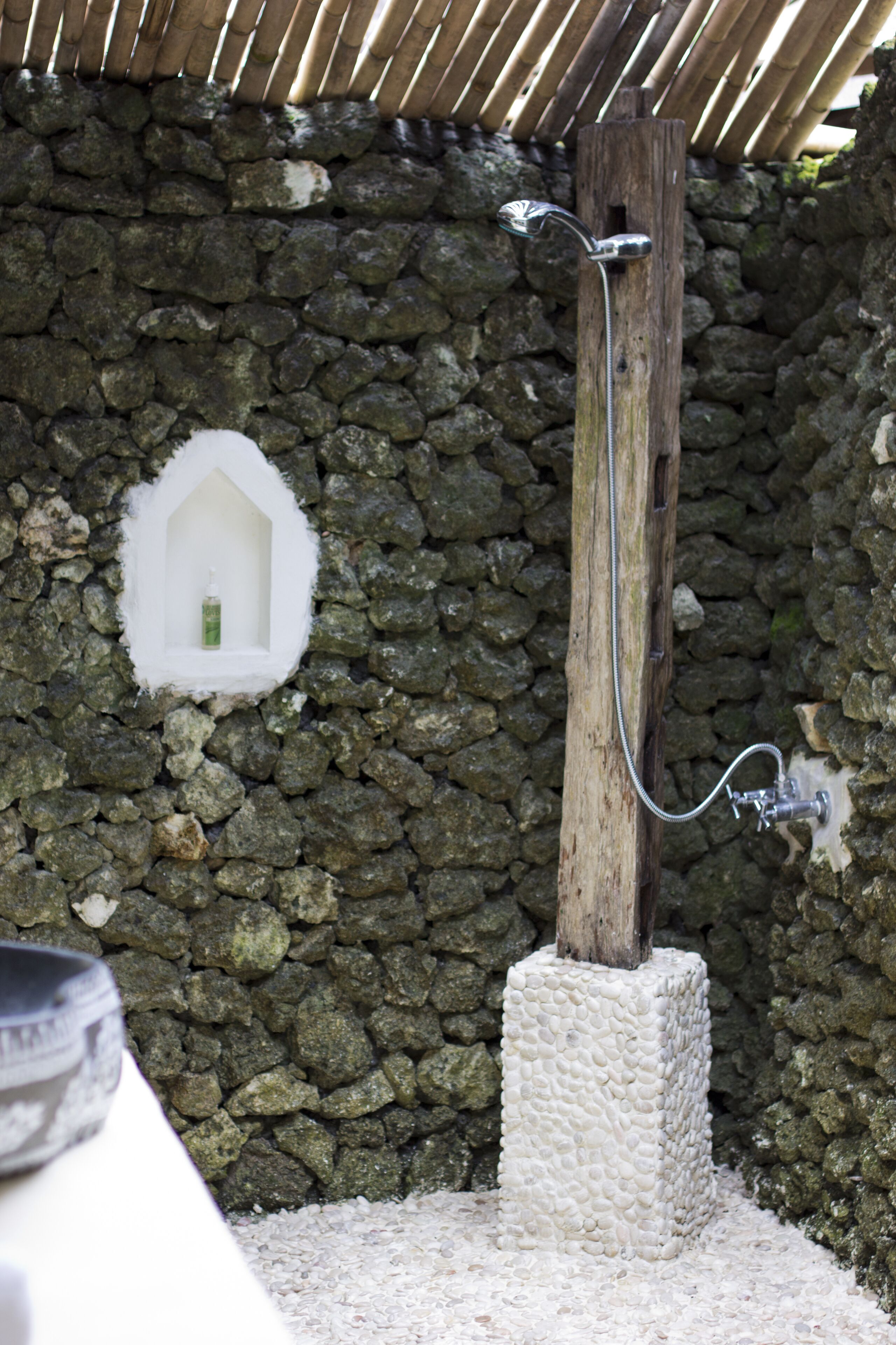 Un mur de pierres avec un poteau en bois et une pomme de douche.