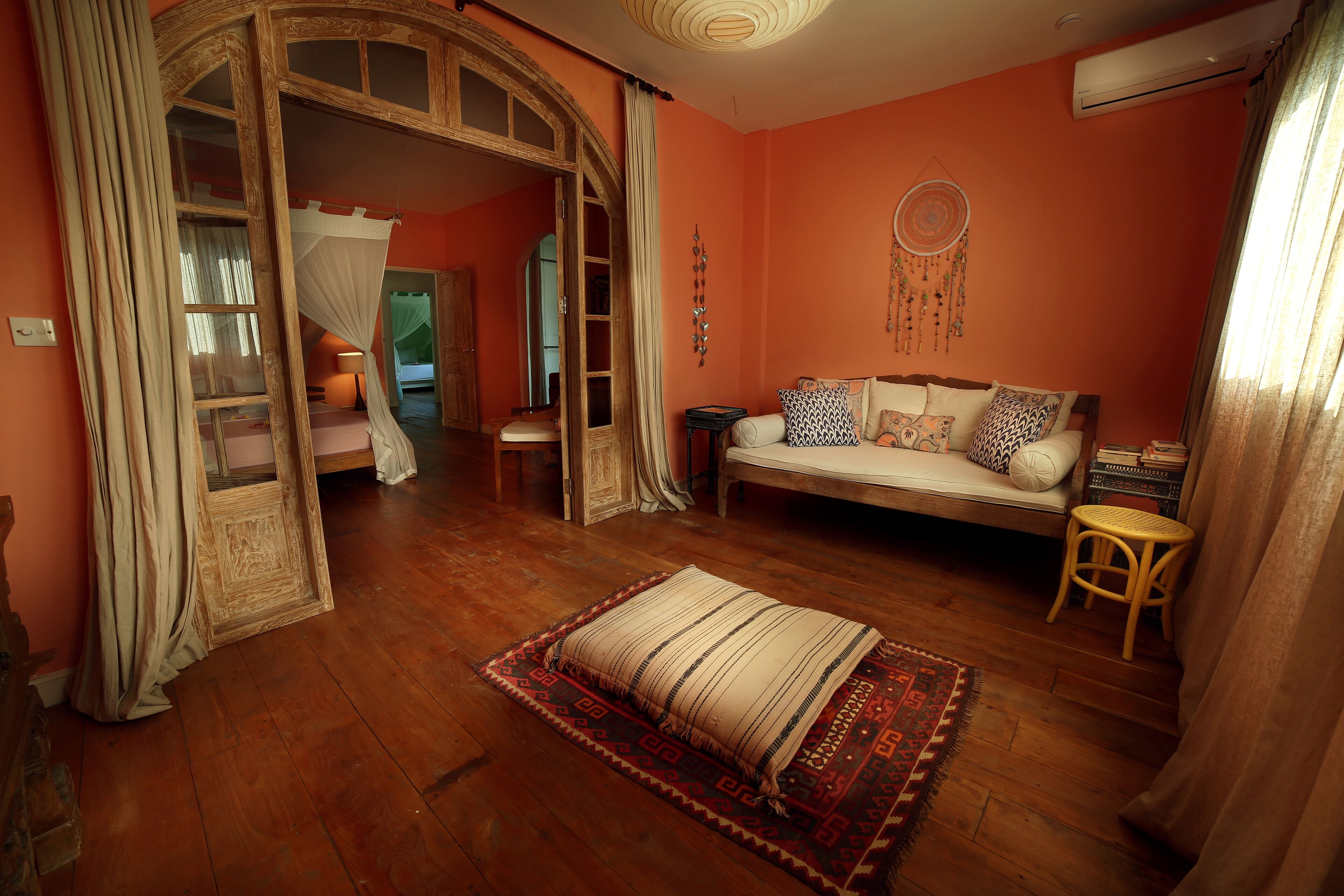 A cozy room with a wooden floor, a sofa with patterned cushions, a small table, and a decorative dreamcatcher.