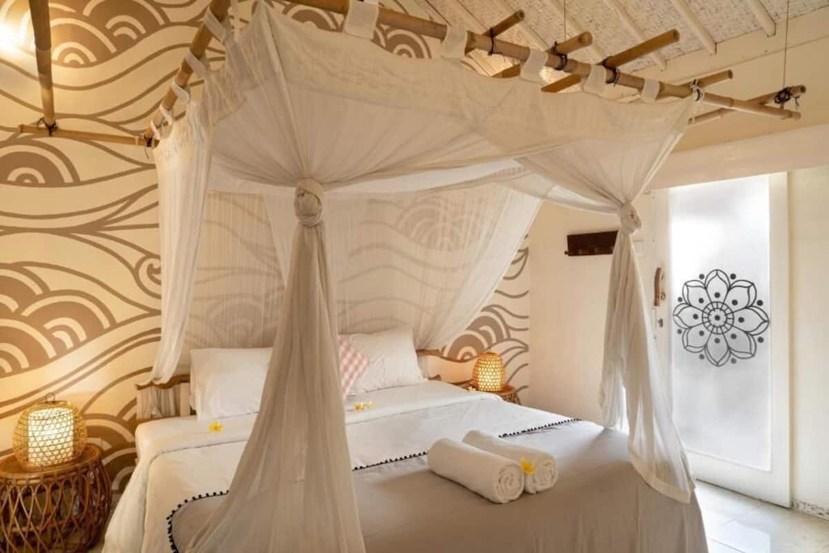 A bedroom with a canopy bed, a decorative wall with a floral pattern, and a bedside lamp.