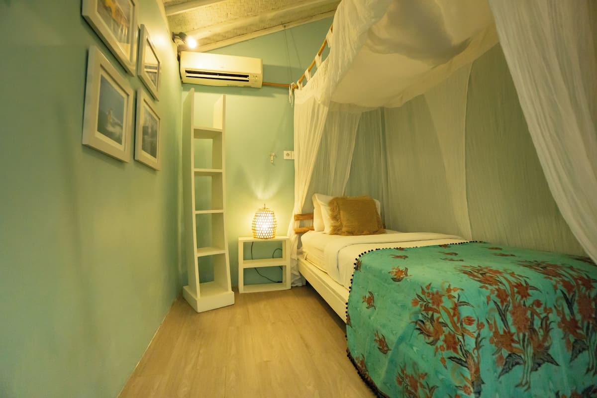 A bedroom with a bed under a canopy, a bedside table with a lamp, and a wall-mounted air conditioner.