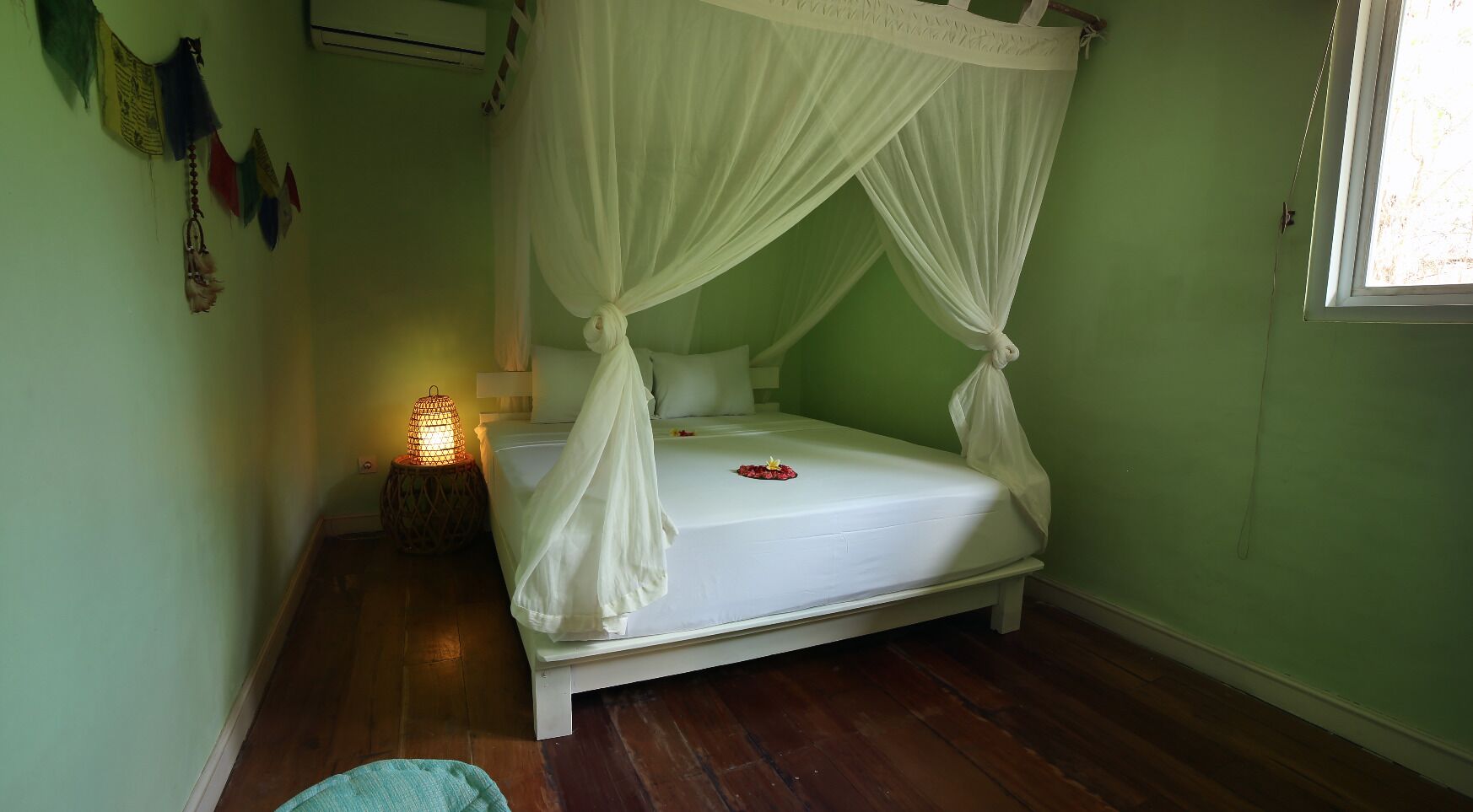 A single bed with a canopy, a bedside table with a lamp, and a window with a curtain.