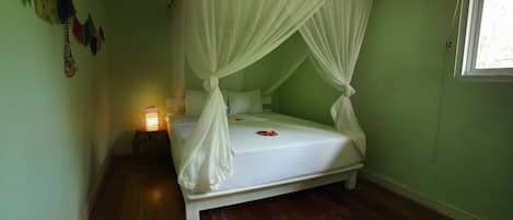 A single bed with a canopy, a bedside table with a lamp, and a window with a curtain.