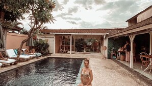 A pool area with a person sitting by the edge, lounge chairs, and a covered patio area. - The Chillhouse Canggu (Canggu)