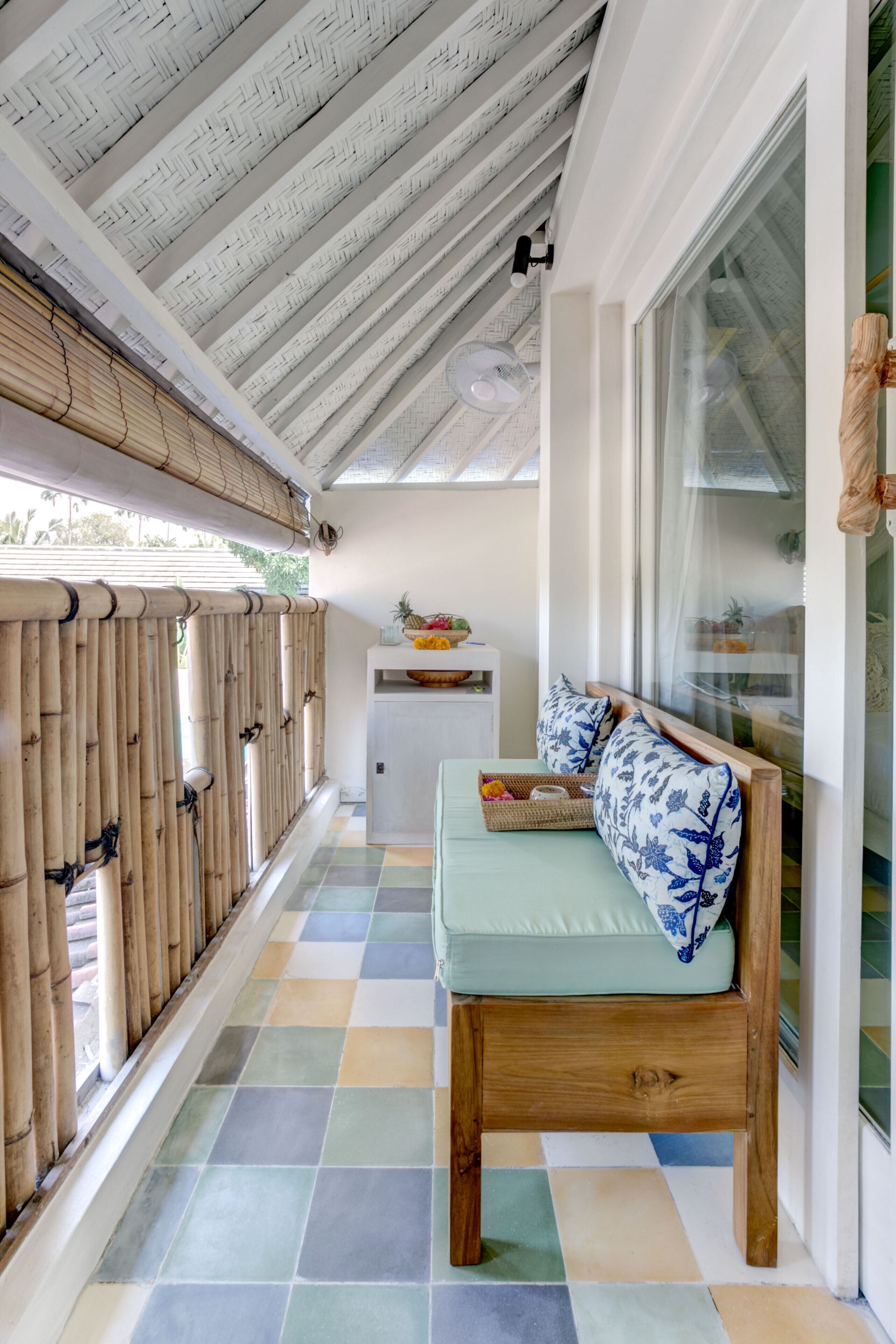 A room with a wooden bench, a small table with a basket, and a window with a view of greenery.