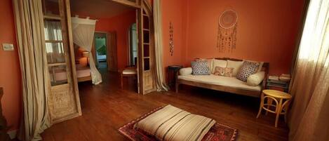 A cozy room with a wooden floor, a sofa with patterned cushions, a small table, and a dreamcatcher on the wall.