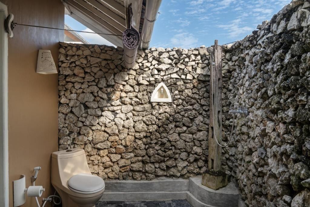 Une salle de bain avec un mur en pierre, des toilettes et un espace douche.