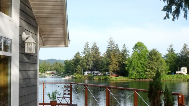 Une terrasse en bois avec une rambarde donnant sur un lac, entourée d’arbres et sous un ciel dégagé.