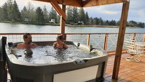 Un bain à remous sur une terrasse en bois, avec vue sur un lac et des arbres.