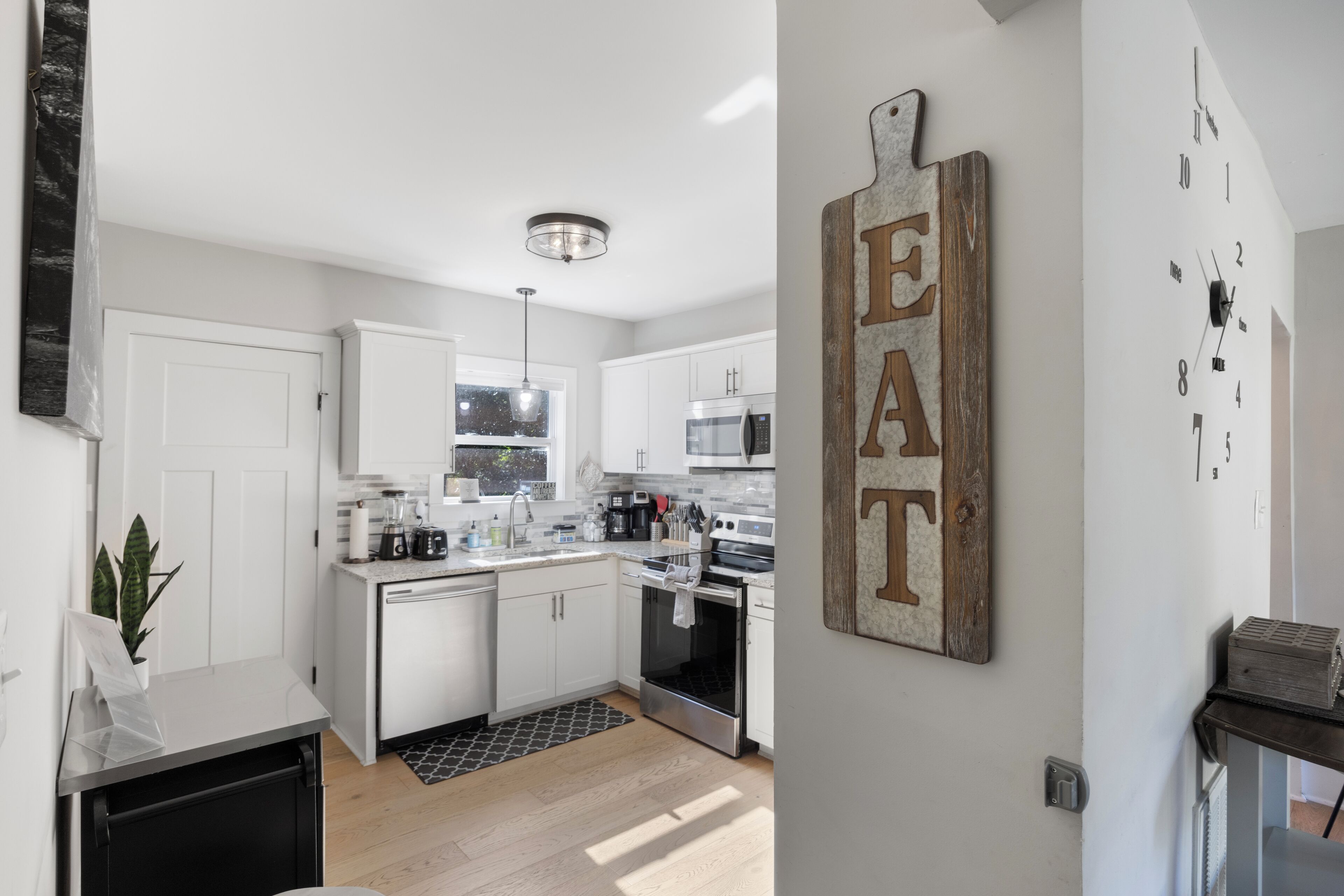 A modern kitchen with white cabinets, stainless steel appliances, and a black and white patterned rug.