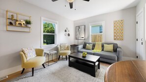 Ein modernes Wohnzimmer mit Deckenventilator, einem grauen Sofa, einem gelben Sessel und einem Couchtisch.
