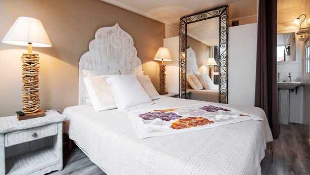 Una camera da letto ordinata con un letto grande, due comodini, uno specchio e un bagno visibile sullo sfondo.