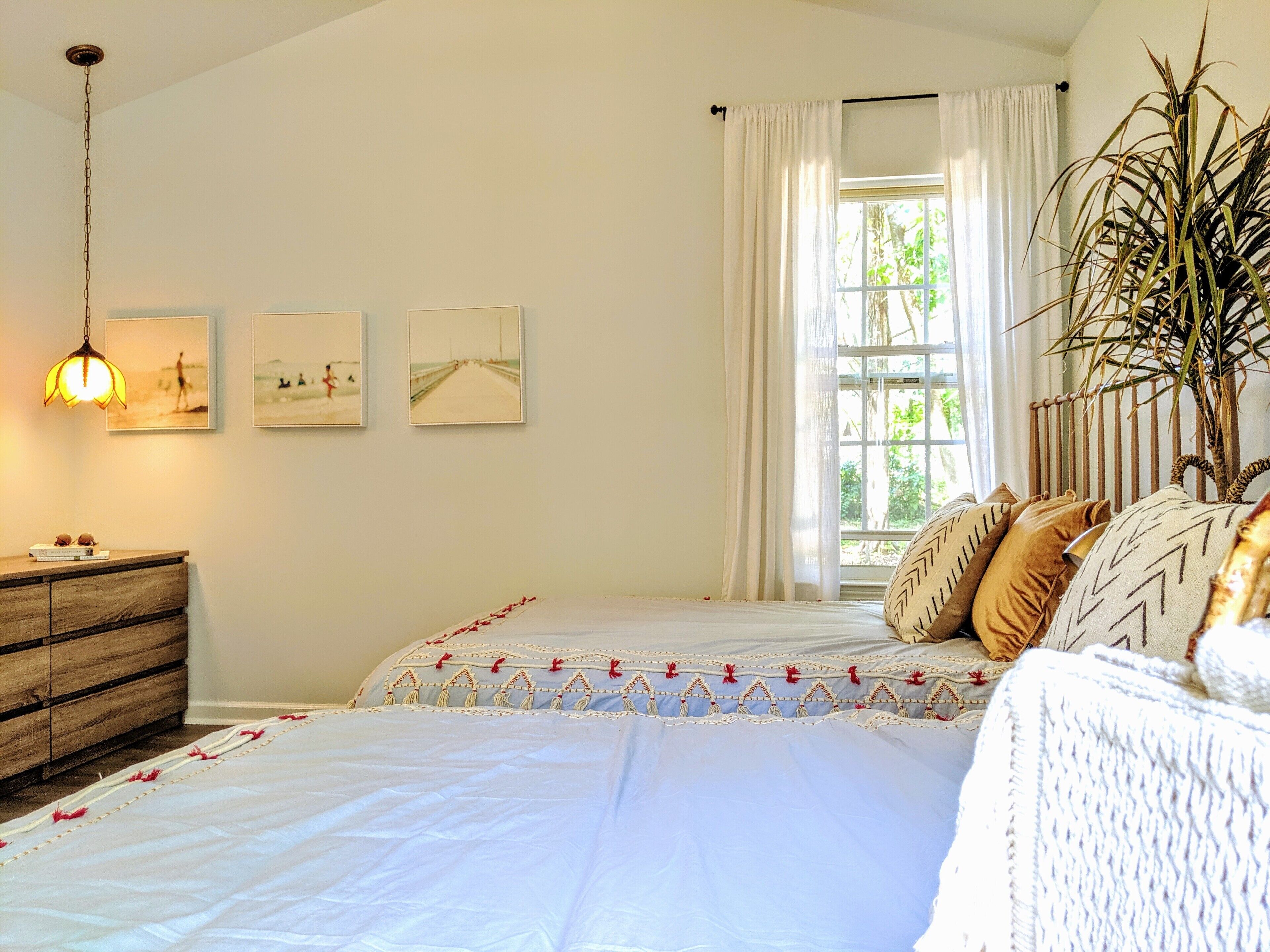 A bedroom with a bed, a dresser, a hanging light, and a window with curtains.