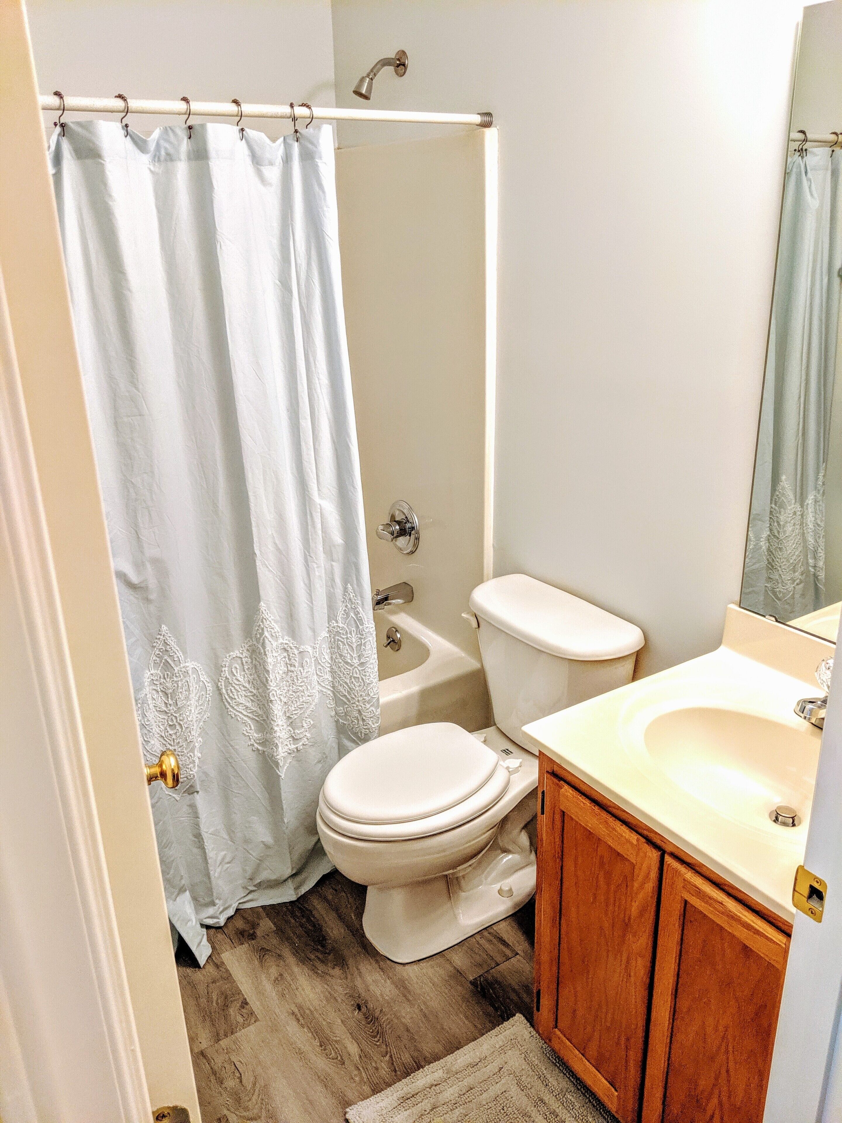 A bathroom with a shower curtain, toilet, sink, and wooden cabinets.