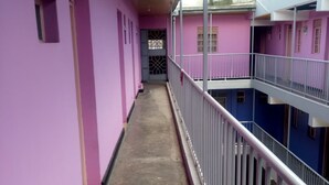 A corridor with pink walls and a concrete floor, leading to a gated entrance. - Witas Lodge (Nakuru)