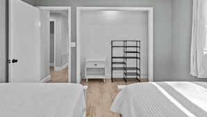Un dormitorio con dos camas, un armario blanco, una estantería metálica negra y una mesita de noche blanca.