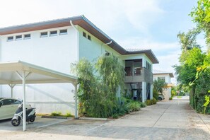 A modern two-story building with a covered parking area and a scooter parked outside.