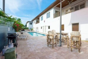A modern outdoor pool area with lounge chairs and a barbecue setup.