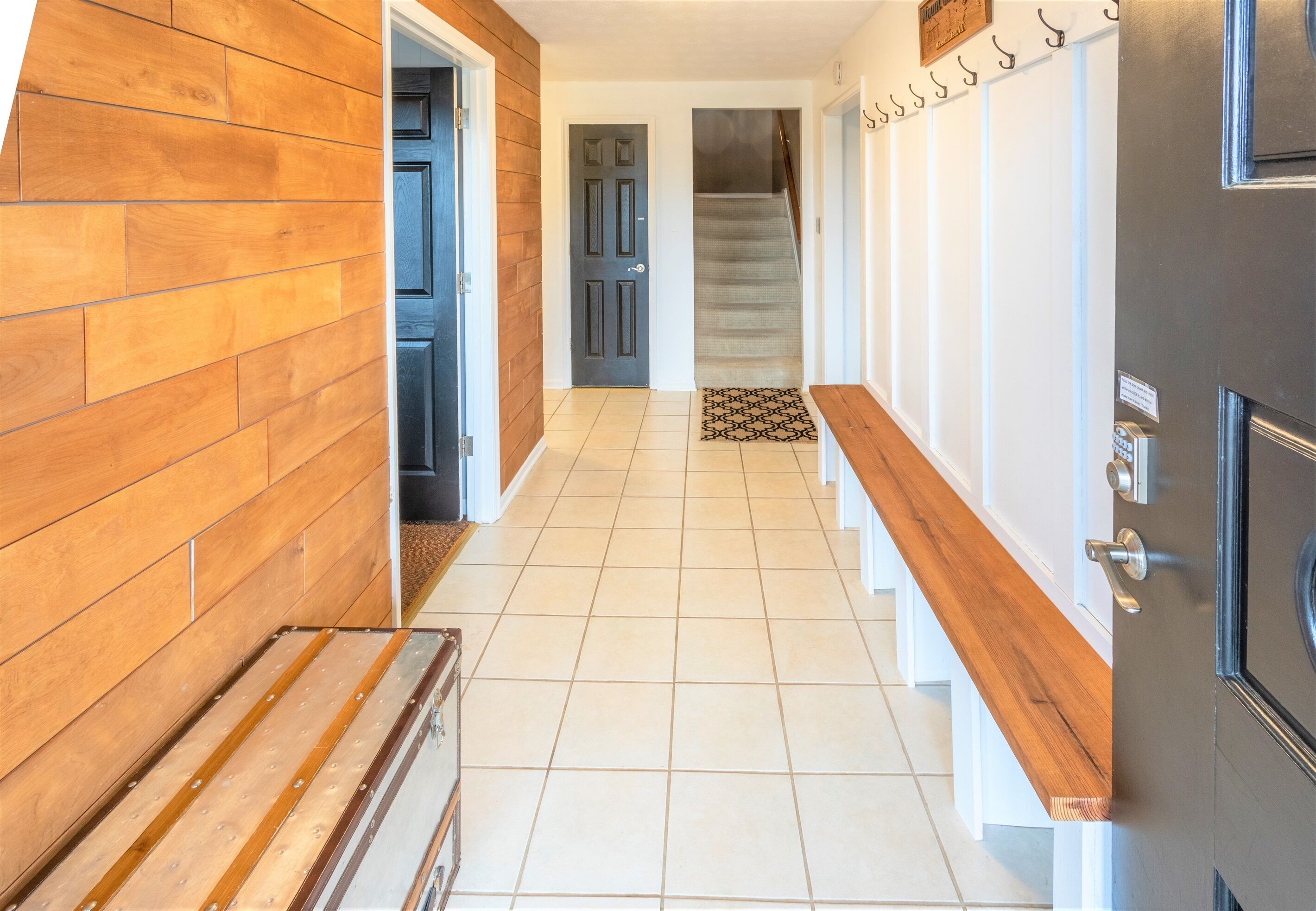 A hallway with wooden walls, a tiled floor, and a staircase leading to another level.
