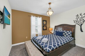 A bedroom with a bed, a television, a window with blinds, a lamp, and a wall decoration.