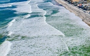 Vista sulla costa con le onde che si infrangono sulla spiaggia sabbiosa e edifici lungo la linea di costa.