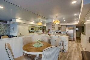Una cucina moderna con isola centrale, una zona pranzo con tavolo rotondo e sedie a righe, e un grande specchio che riflette l'ambiente.