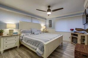 Una camera da letto con un letto, comodini, una ventola a soffitto e una finestra con persiane.