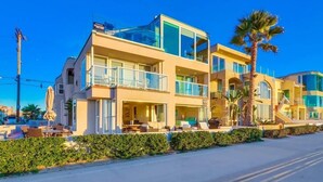 A modern two-story hotel with a balcony, outdoor seating, and a palm tree.
