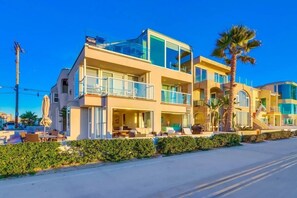 A modern two-story hotel with a balcony, outdoor seating, and a palm tree.