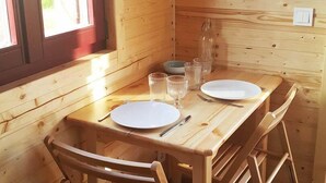A wooden cabin interior with a dining table set for two, a window, and a wall-mounted light switch. - La Pouypardin, a caravan for a cosy stay (CONDOM)
