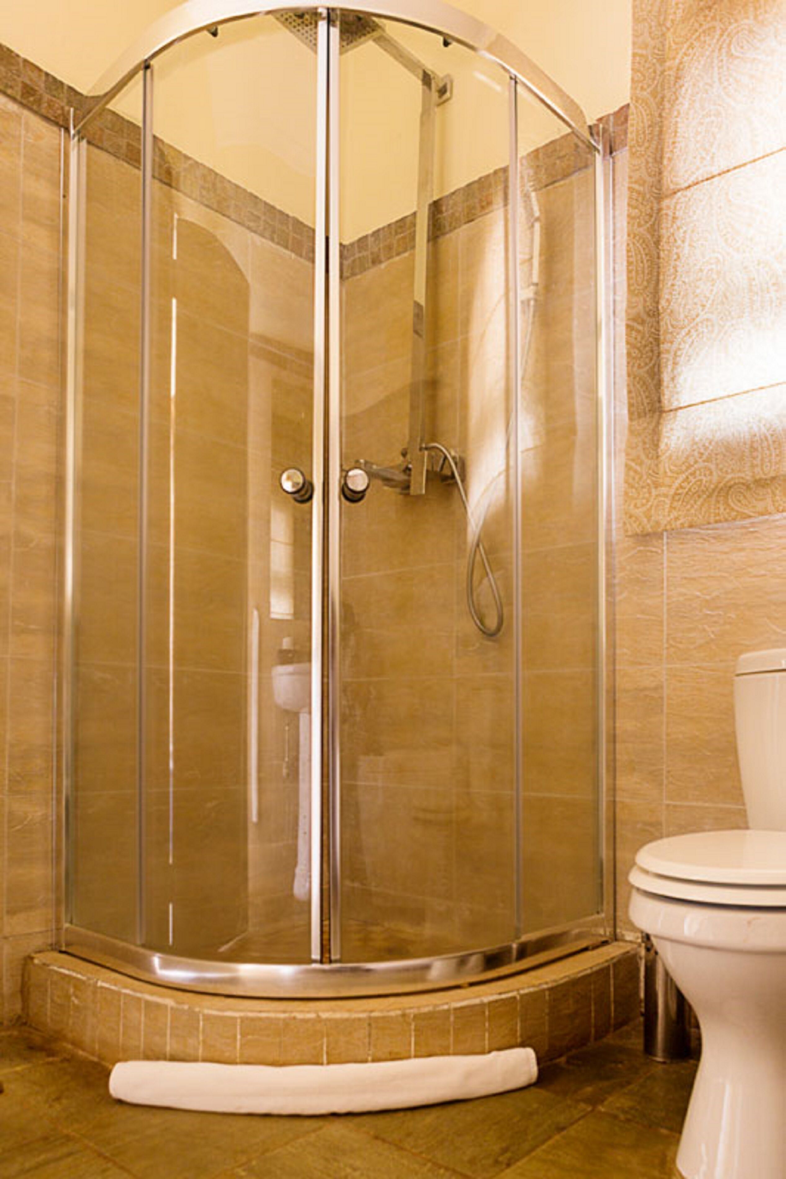 A glass-enclosed shower stall with a curved design, a toilet, and a patterned wall.