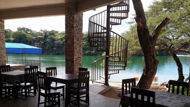 A covered outdoor seating area with tables and chairs, a spiral staircase, and a view of a lake. - Tiffany s Canyon lodge (Kafue)