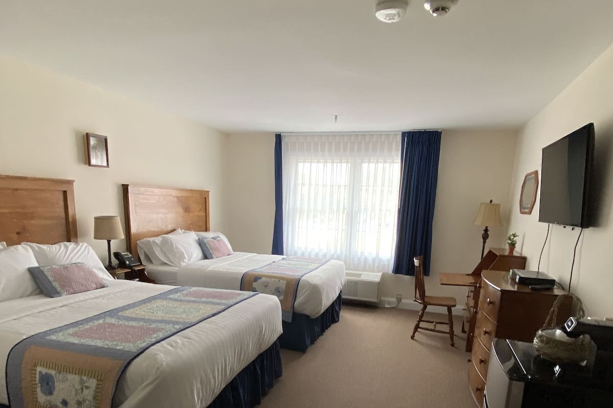 Habitación de hotel con dos camas, un escritorio, una silla, un televisor y una ventana con cortinas.