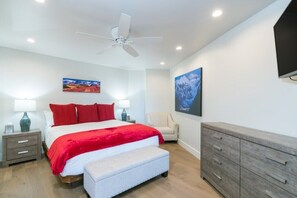 Een moderne slaapkamer met een bed, nachtkastjes, een stoel, een dressoir en kunst aan de wanden.