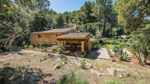 Una casa de piedra rústica con tejado de baldosas, rodeada de árboles frondosos y un jardín con plantas en macetas.