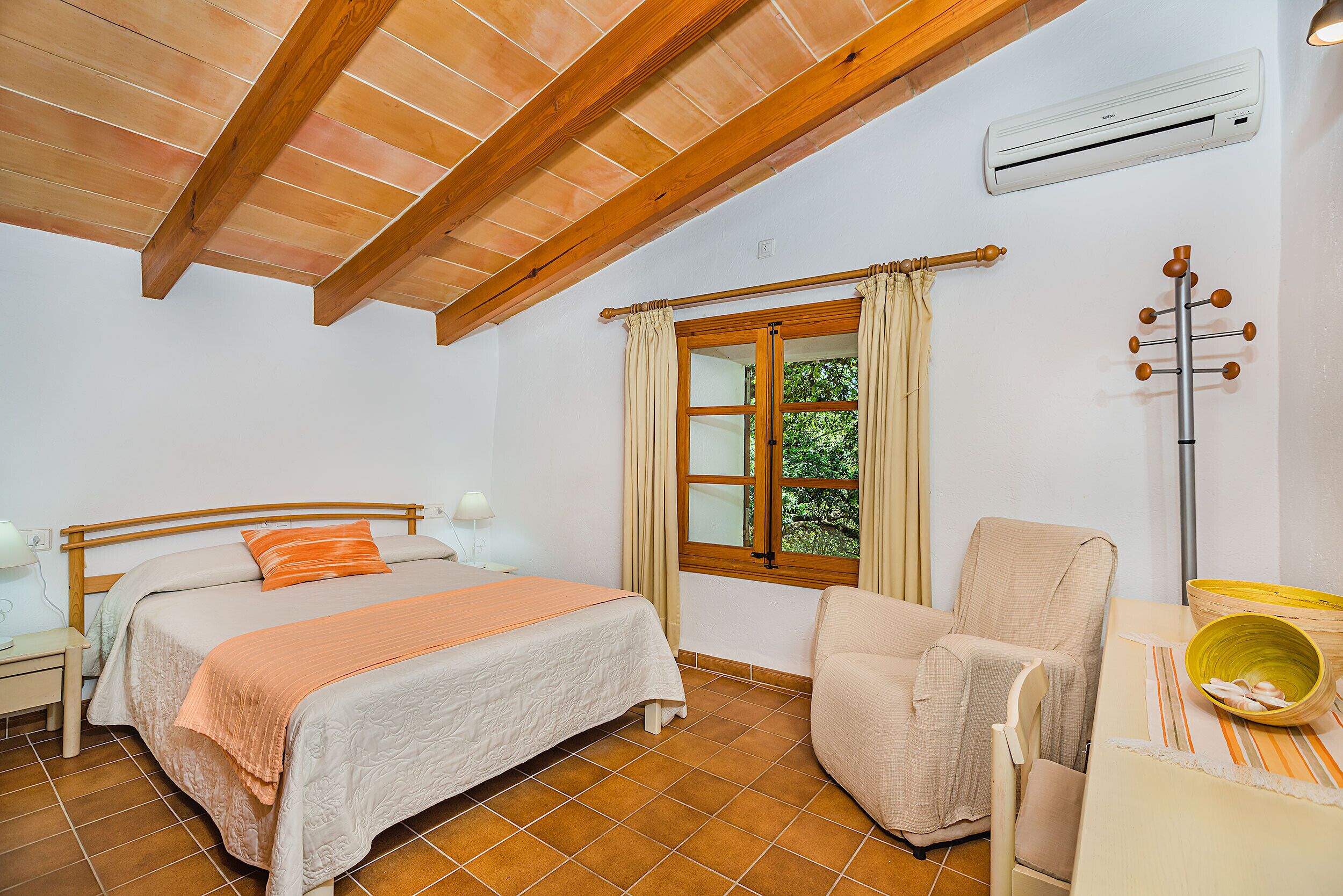A bedroom with a bed, a chair, a window, and an air conditioning unit.