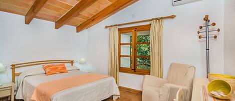 A bedroom with a bed, a chair, a window, and an air conditioning unit.