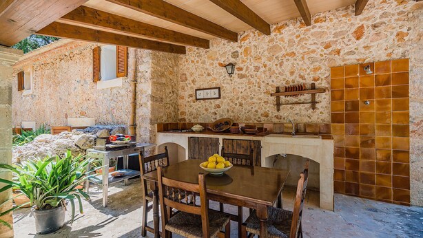 Una cocina rústica de piedra con vigas de madera, pared de piedra y salpicadero de azulejos.