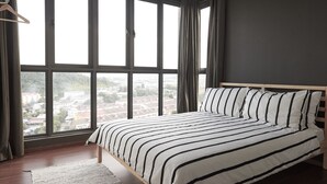Un dormitorio con un ventanal grande, una cama con ropa de cama a rayas y vistas a un paisaje urbano.