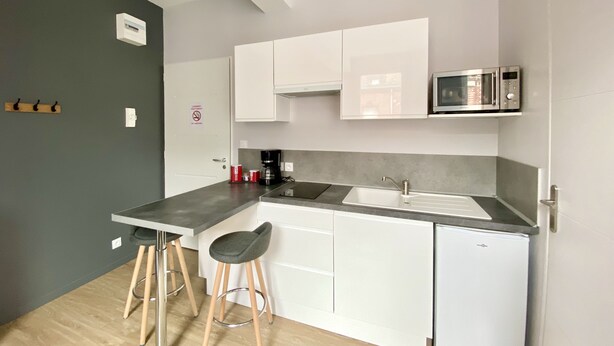 A compact kitchen with a sink, a microwave, and a coffee maker. There are two stools and a door with a sign. - Comfortable studio near University of Artois (Arras)