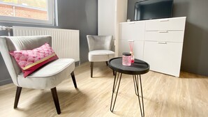 A modern room with a white armchair, a small round table with a pink candle, a white cabinet, and a television on a stand. - Comfortable studio near University of Artois (Arras)