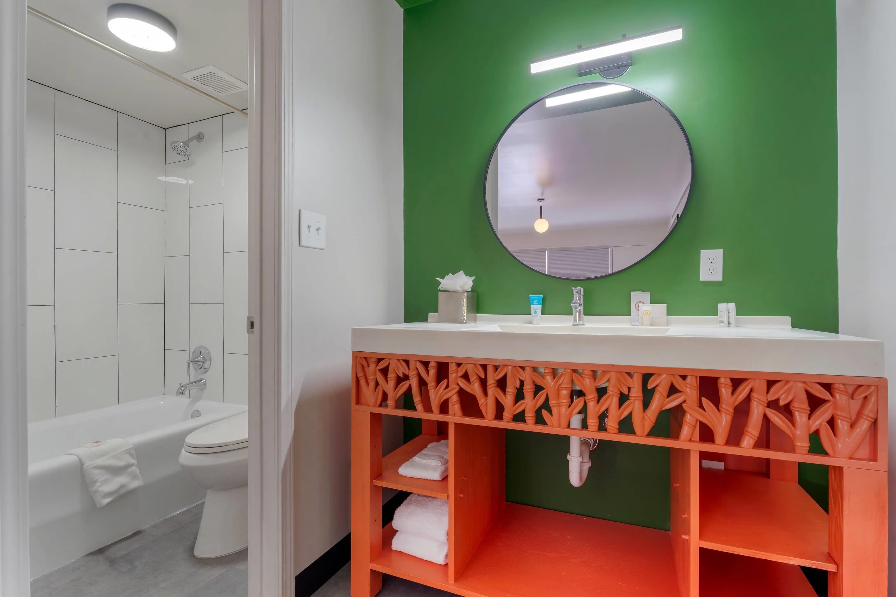 A bathroom with a white bathtub, a white sink with a mirror above it, and a green accent wall.
