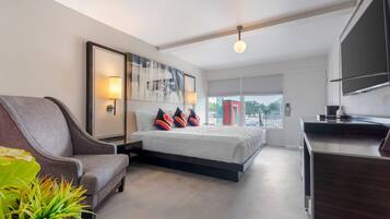 A modern hotel room with a bed, a sofa, a TV, and a large window.