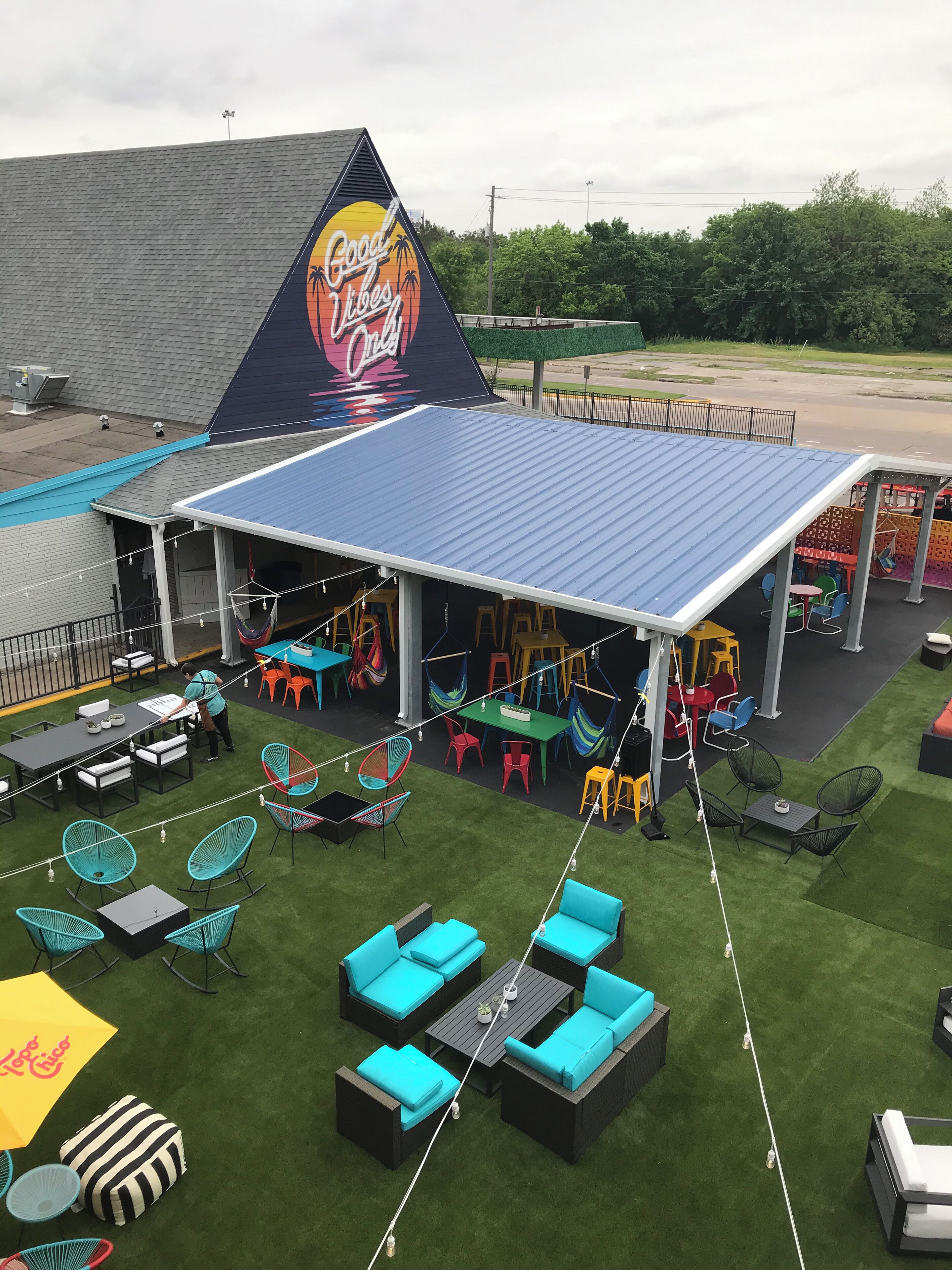 Un espace extérieur aménagé avec plusieurs tables et chaises, une terrasse couverte et une grande fresque sur le mur du bâtiment.