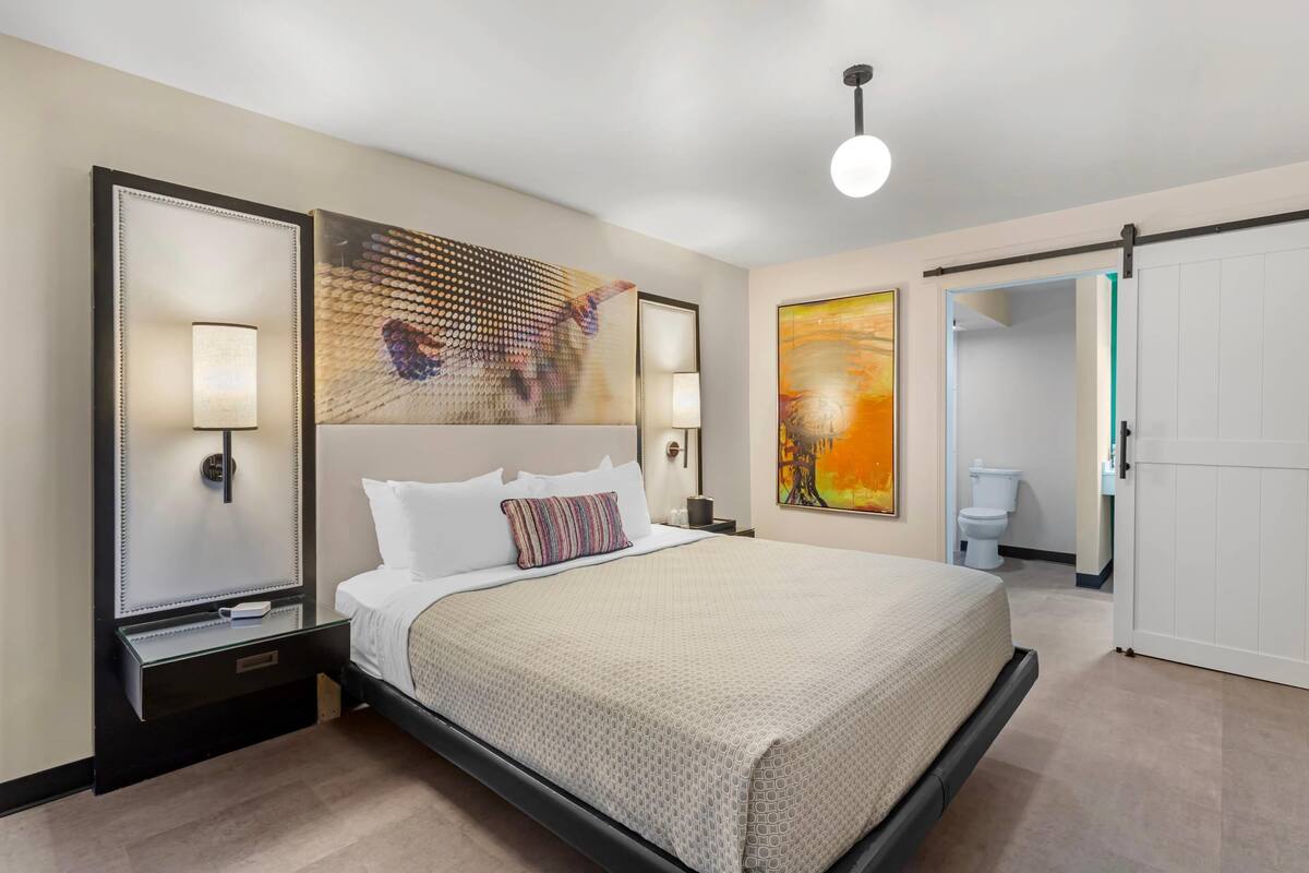 A modern hotel room with a large bed, bedside lamps, a flat-screen TV, and artwork on the walls.