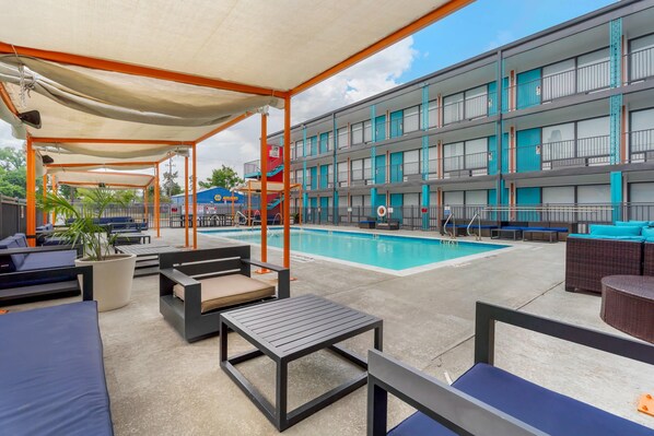 A hotel with a swimming pool, outdoor seating, and a covered area.