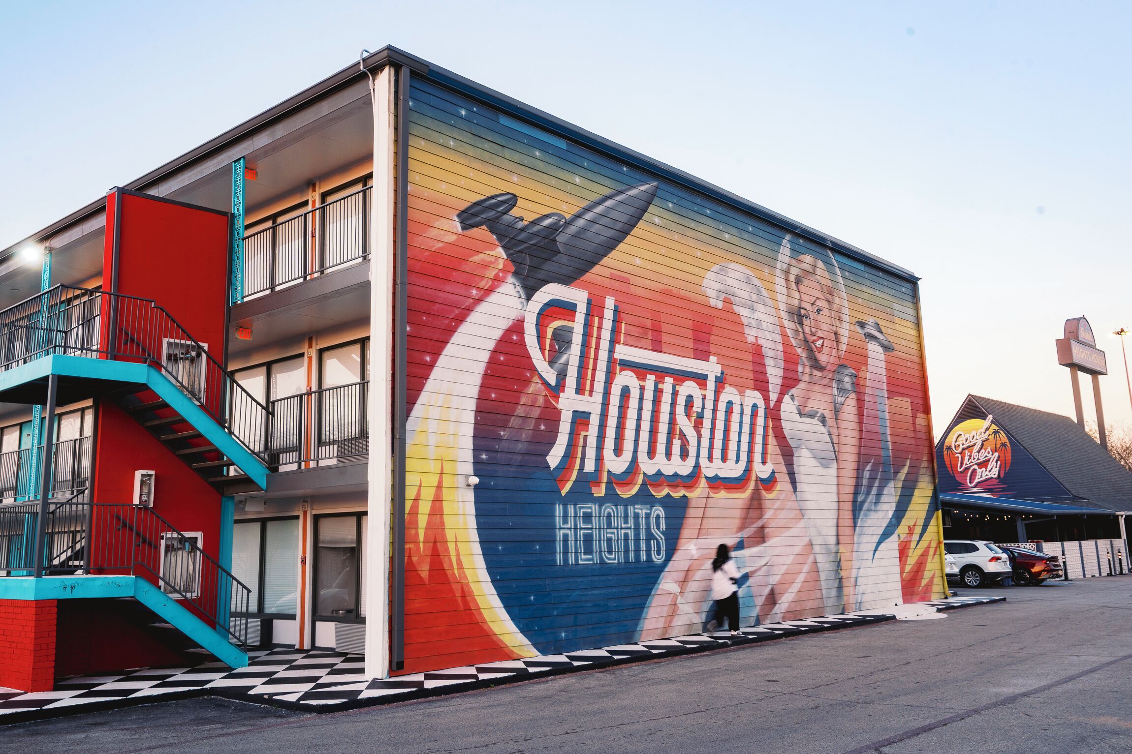 Un edificio con un mural de una mujer y un hombre, el nombre 'Houston Heights' en la fachada, y una escalera que conduce a un nivel superior.